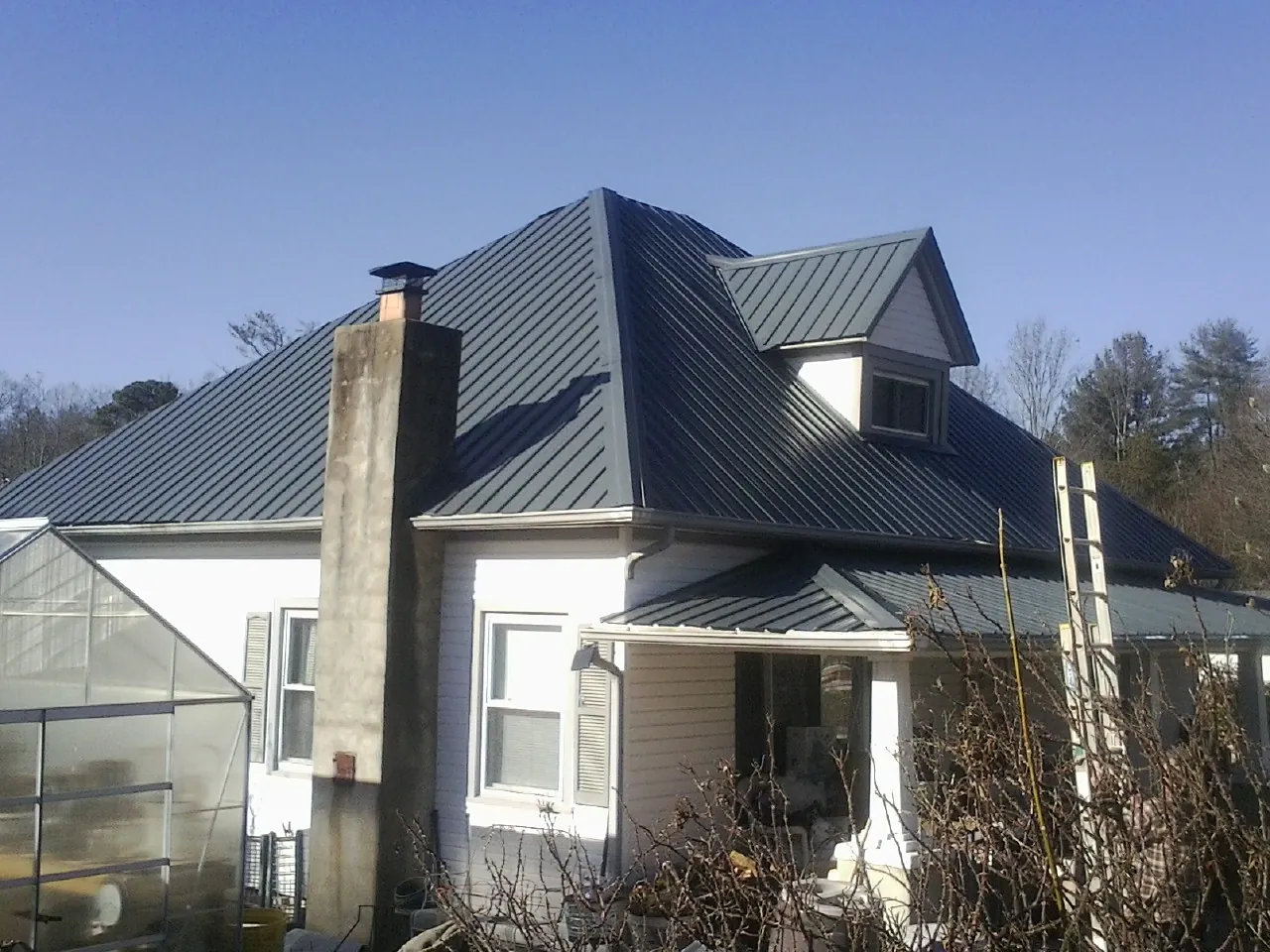 Dark blue standing seam metal roof on a white farmhouse with dormer — Slate & Tile Roof Repair by Roofing Brothers in Des Moines