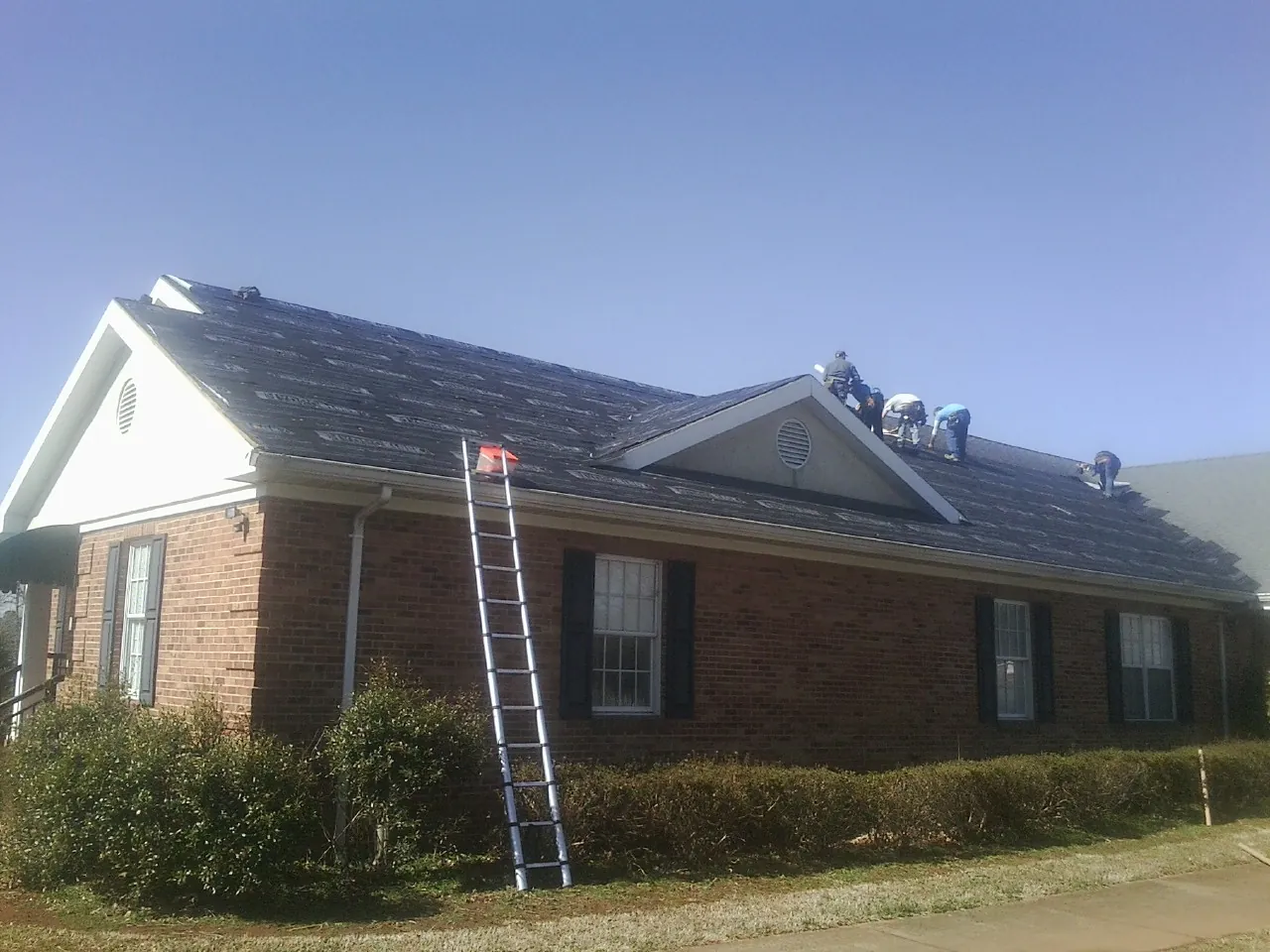 Crew tearing shingles off a brick ranch roof with a ladder set — Emergency Roof Repair work by our crew in Des Moines