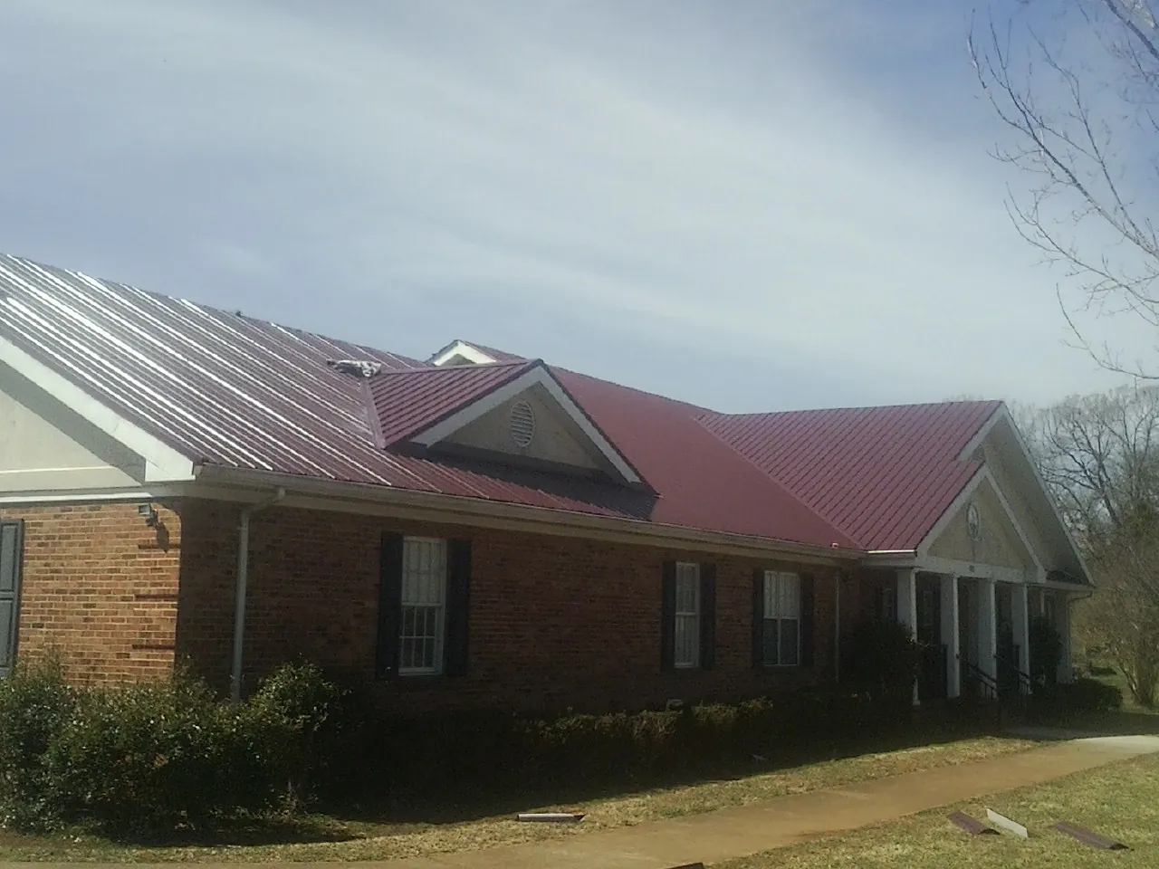 Red metal roof with gabled entries on a long brick building, from a Hail Damage Roof Repair job in Des Moines