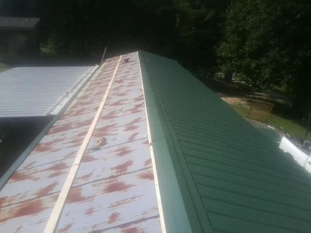 Old rusted panels beside newly installed green metal roofing — Wind Damage Roof Repair by Roofing Brothers in Des Moines