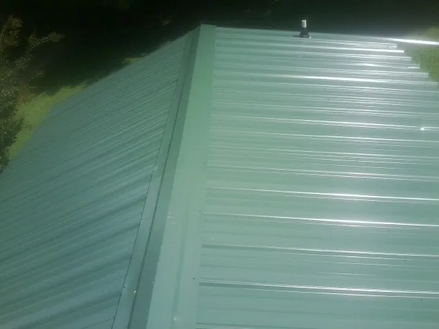 New green metal panels meeting at the ridge of a roof — Flat Roof Repair work by our crew in Des Moines
