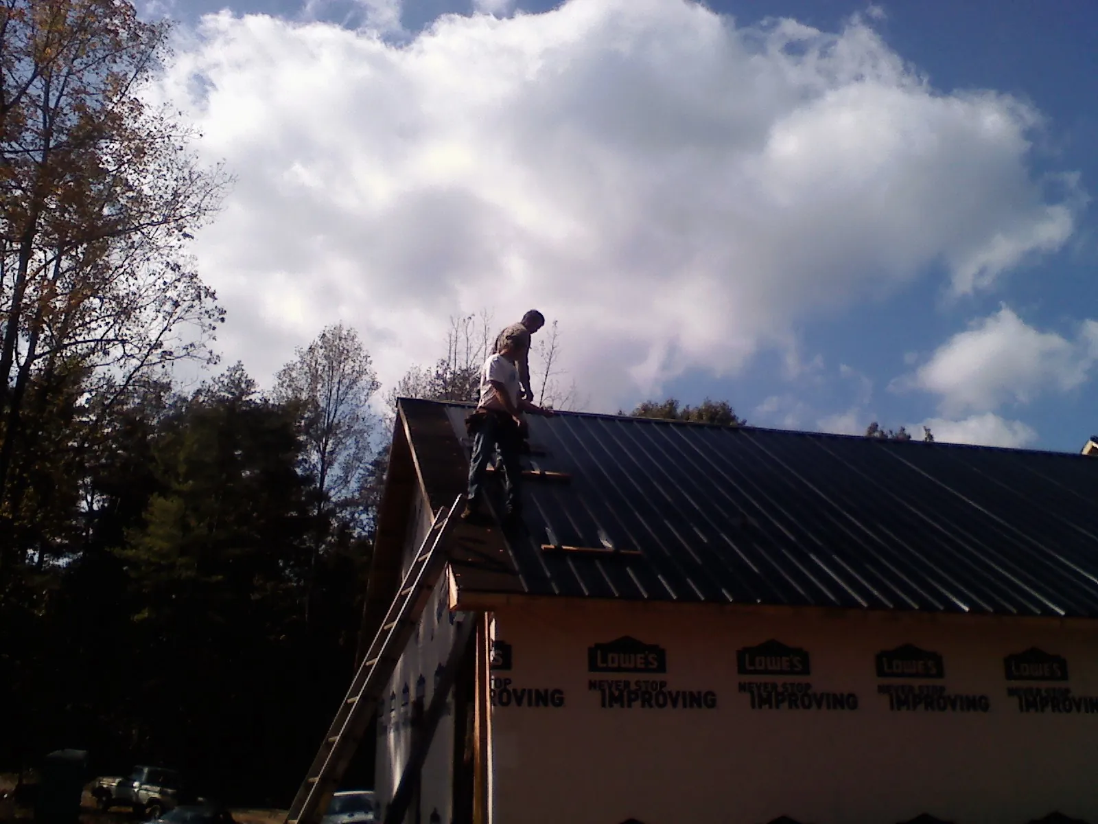 Roofer fastening dark metal panels high against a cloudy sky, from a Roof Inspection job in Des Moines