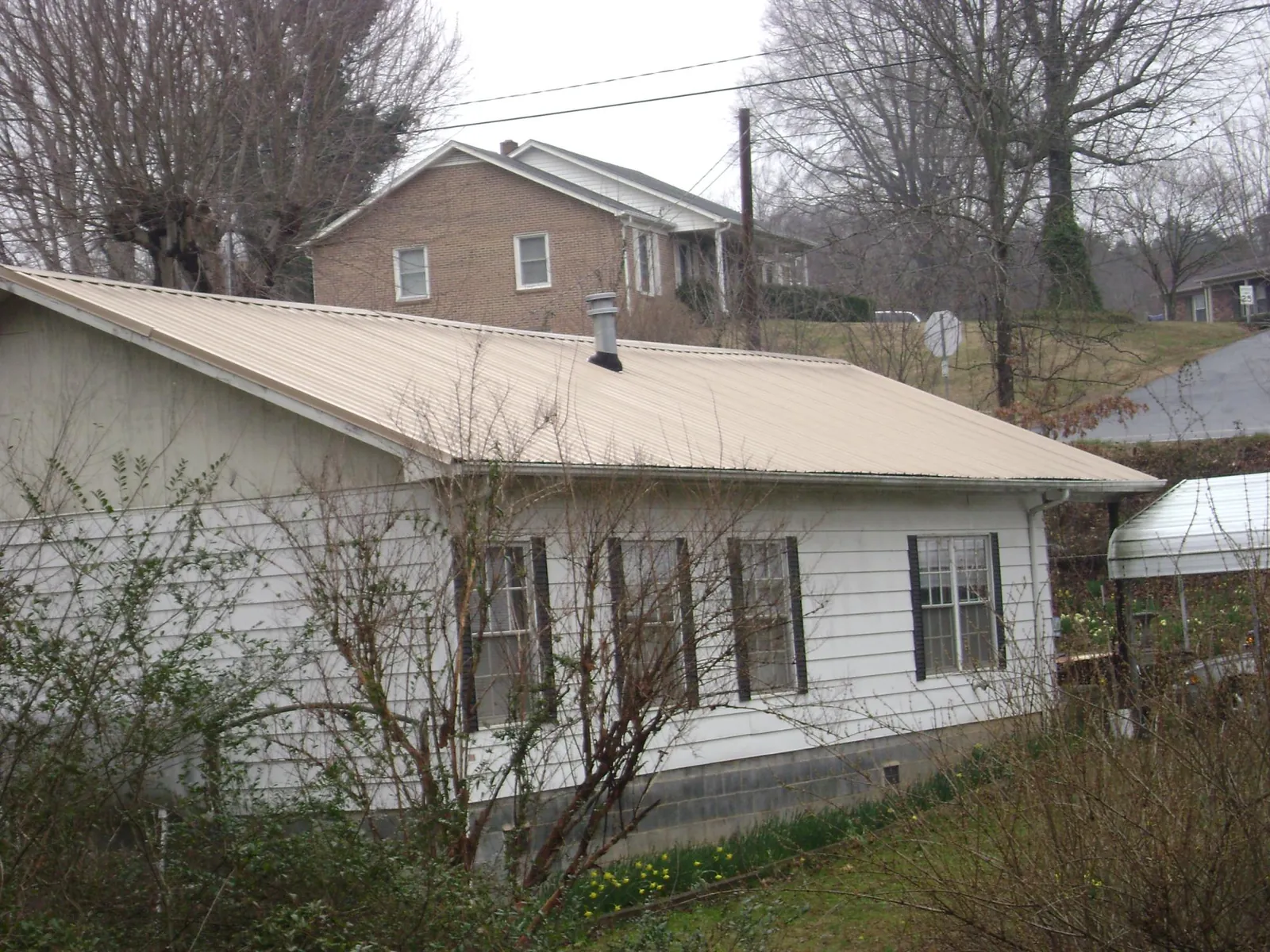Tan metal roof on a white sided house set into a hillside — Commercial Roofing by Roofing Brothers in Des Moines