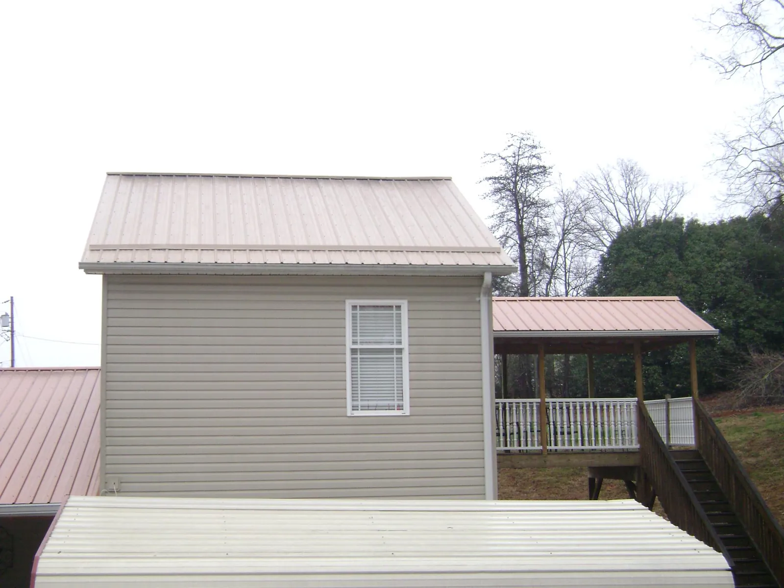 Tan metal roofs on a two story addition and attached porch, from a Roof Replacement job in Des Moines