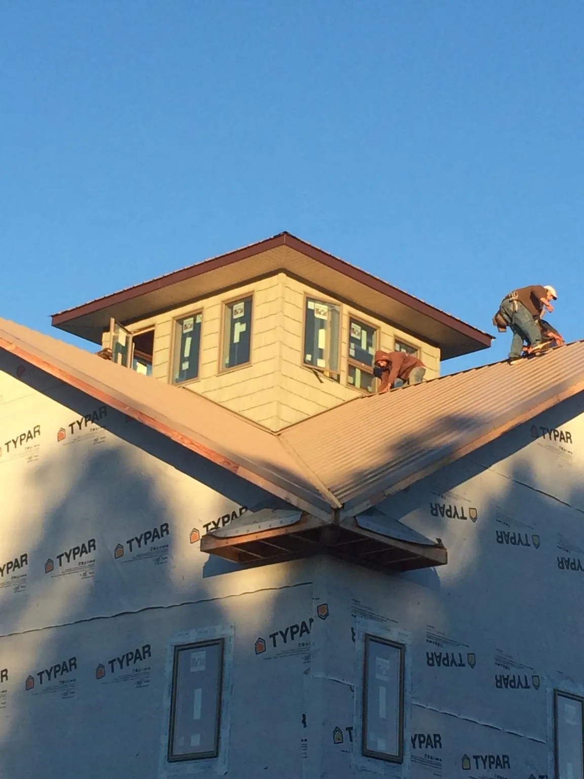 Roofers working around a rooftop cupola on a new metal roof at sunset — Roof Waterproofing in Des Moines by Roofing Brothers